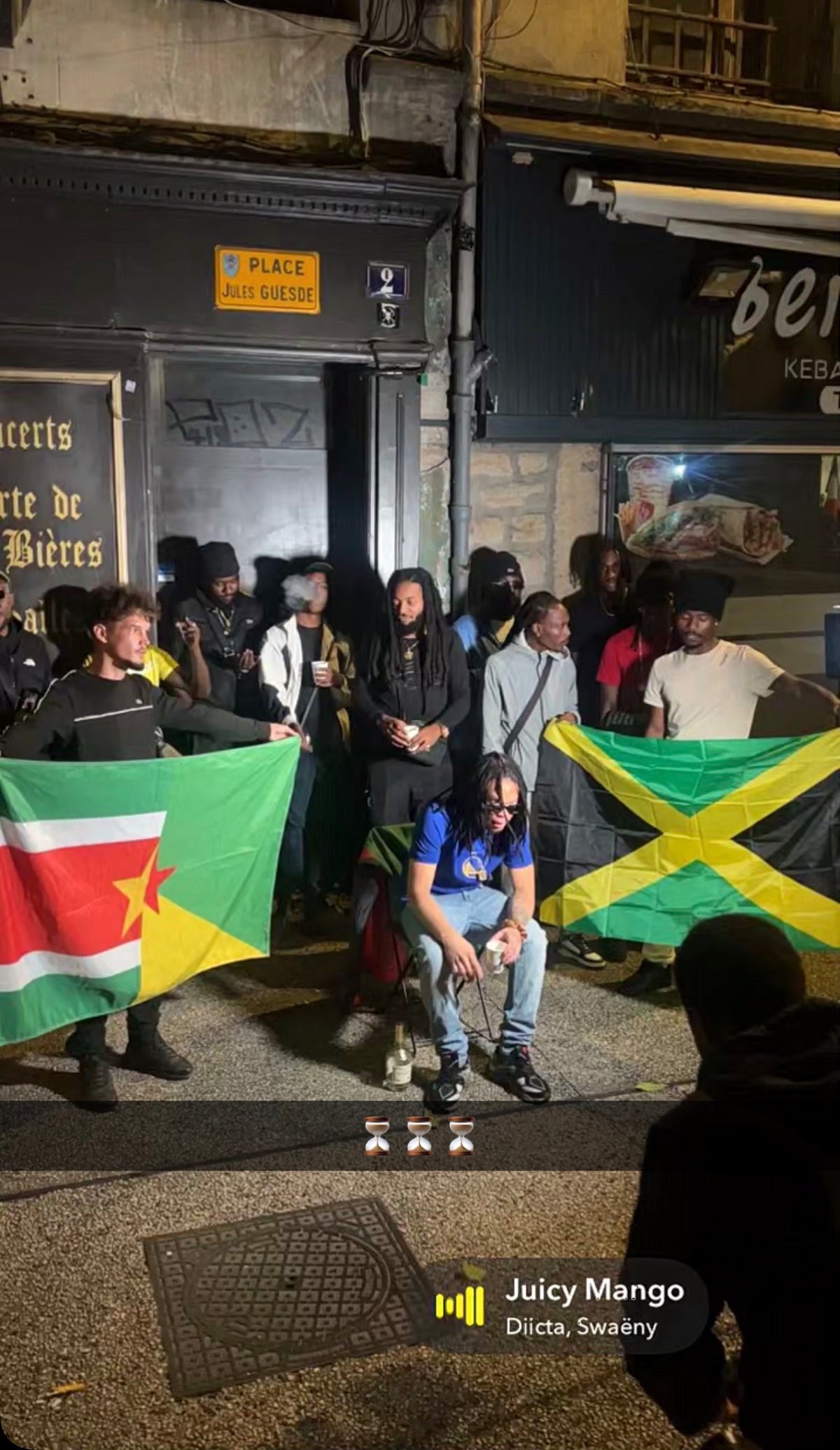 Groupe présentant plusieurs drapeaux, dont un drapeau jamaïcain, lors d’un rassemblement en soirée.