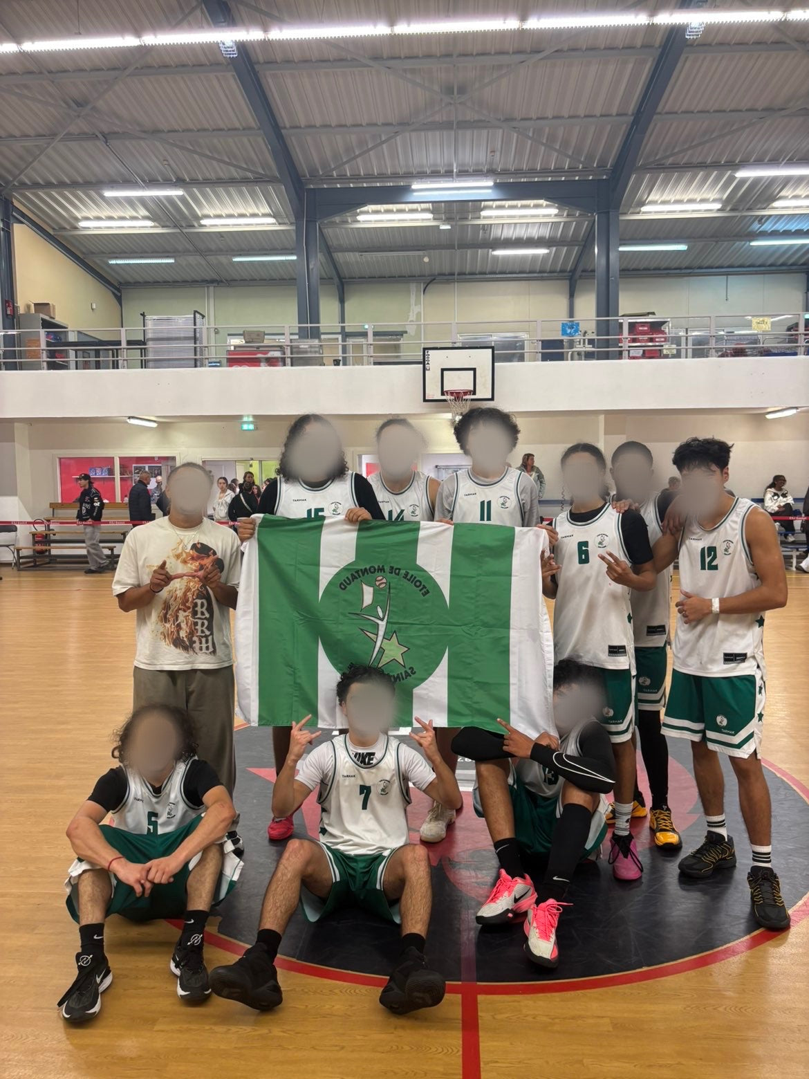 Équipe de basketball en tenues blanches et vertes présentant un drapeau personnalisé au logo du club.